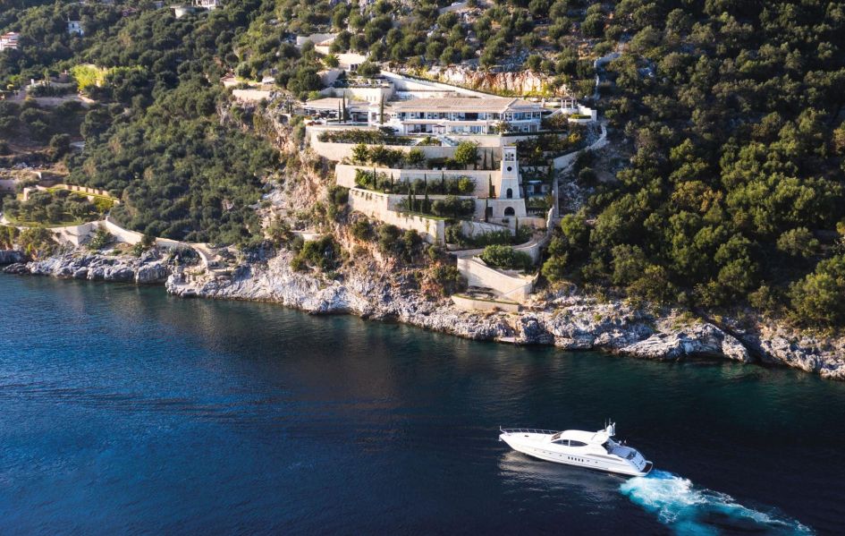 A drone shot of Ultima Corfu, a stunning Greek Island villa built into the cliffs with the sea in the foreground with a boat.