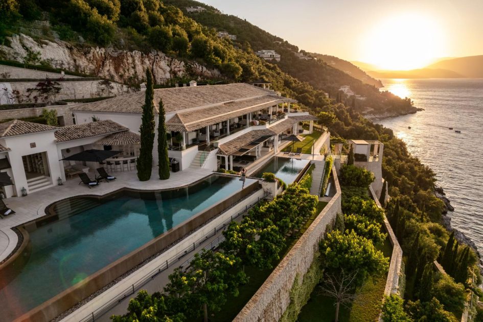 A drone shot showing two swimming pools overlooking the sea at Ultima Corfu, a luxury villa with a pool in Greece. It is built into the cliff and has a sunset view.