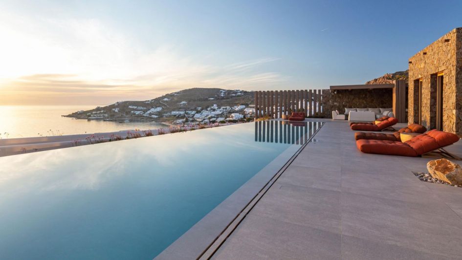 A stunning outdoor pool with a view of the sunset in Mykonos at one of the best luxury Greek Island villas, Villa Phantom. There are sun loungers and views over the sea.