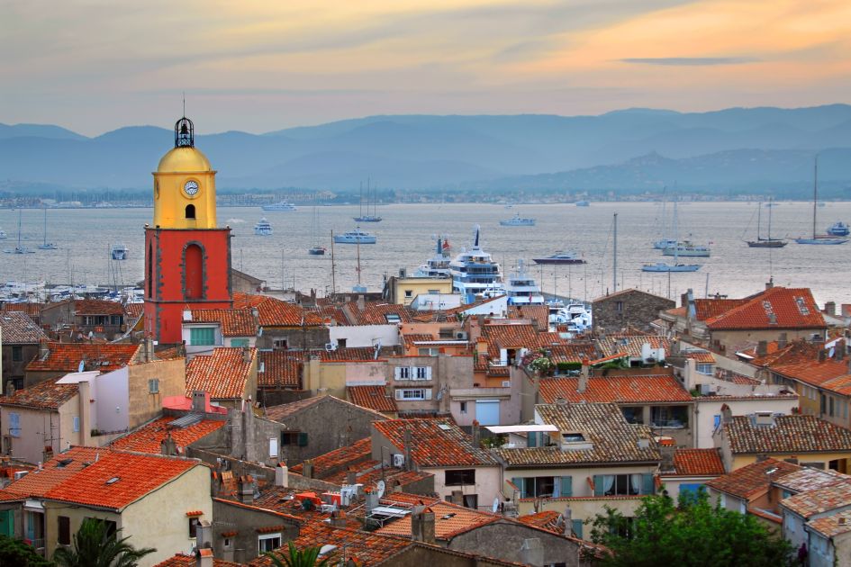 View of St Tropez traditional buildings at sunset with luxury yachts and boats in the background. 