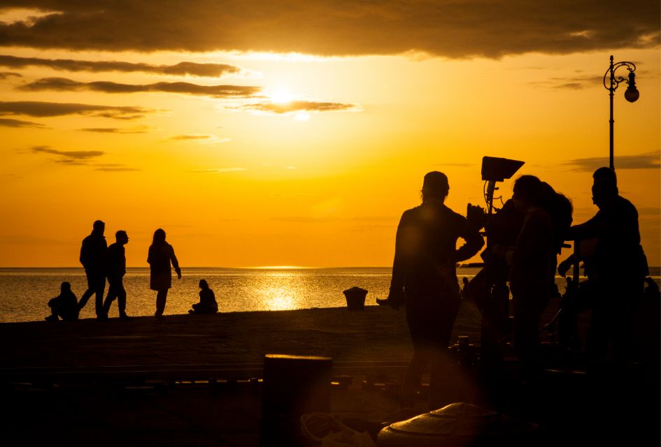 Set Jetting Destinations. Credit: bepslabor via Canva Photos Sunset with silhouettes of people filming a movie with the ocean in the distance, a visual you could see on a set jetting villa holiday.