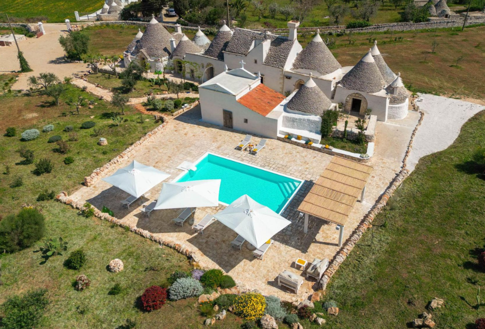 Masseria Le Monache, Puglia, Italy View from above of Masseria Le Monache, a unique luxury villa with trulli houses and their domed roofs forming the residence, and a modern outdoor swimming pool, surrounded by the Italian countryside.