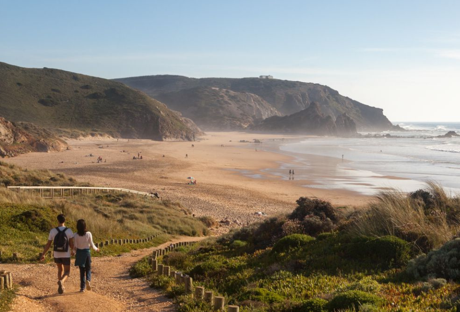 Aljezur Amado beach (Credit: AT Algarve) Couple walking down the footpath to Amado Beach on a luxury Algarve holiday, before rugged golden cliffs, expansive sands and lapping waters.