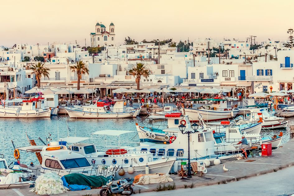 Boats moored and busy restaurants along the waterfront of Naousa harbour, with a background 'maze' of white buildings - a classic reflection of what luxury holidays in Paros look like! 