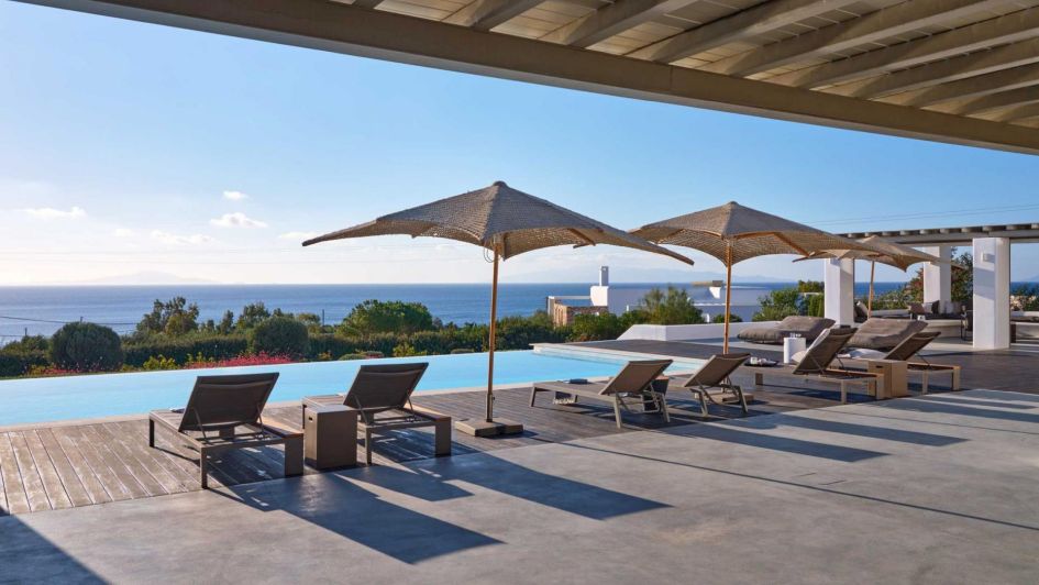 Villa Ametista's terrace with views of Lolantonis Beach visible past the loungers, infinity pool and outdoor relaxation areas.