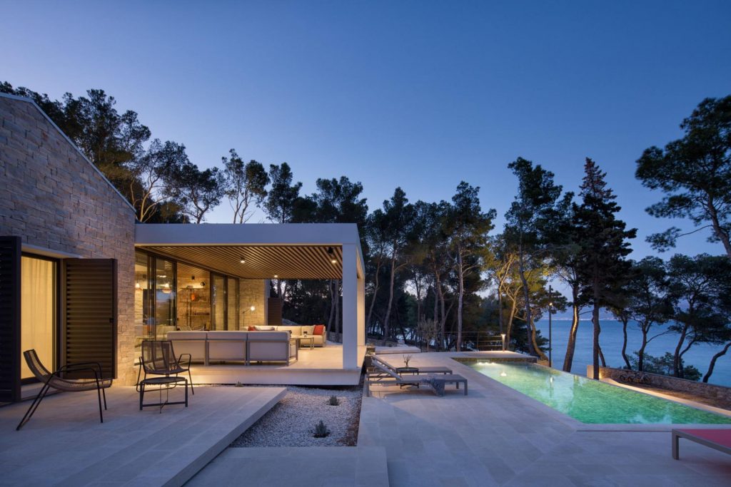 Villa Sea Gem, Croatia's Islands Pool and terrace at luxury villa rental Sea Gem on the island of Brač at dusk. Surrounded by trees and illuminated by lights from the villa and swimming pool.