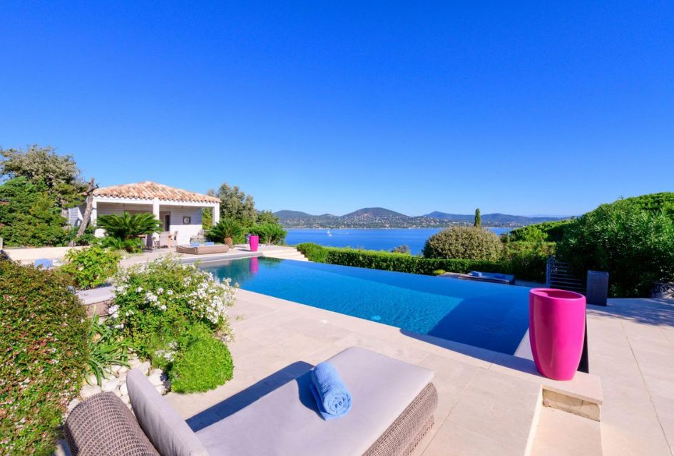 Outdoor pool at Villa Rêve de Lumière, looking out at the ocean and coast of tge French Riviera, pool house to one side and sun loungers in the foreground.